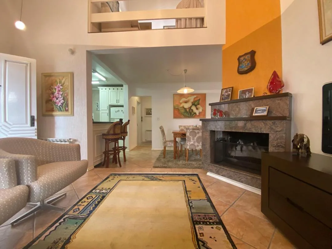 Sala com lareira revestida em pedra, parede laranja e mezanino aberto sobre o ambiente