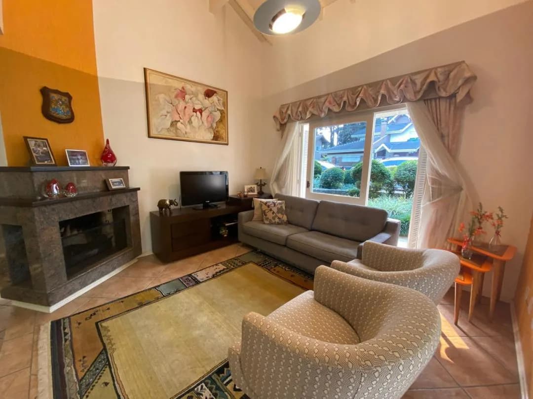 Sala com sofá cinza junto à janela, poltronas giratórias e lareira com porta-retratos sobre o consolo
