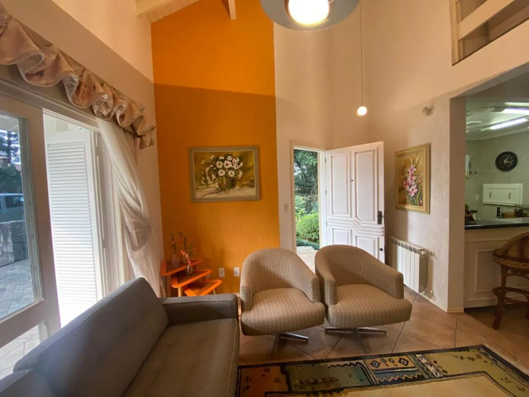 Sala com duas poltronas giratórias, parede laranja e porta de entrada aberta para o jardim