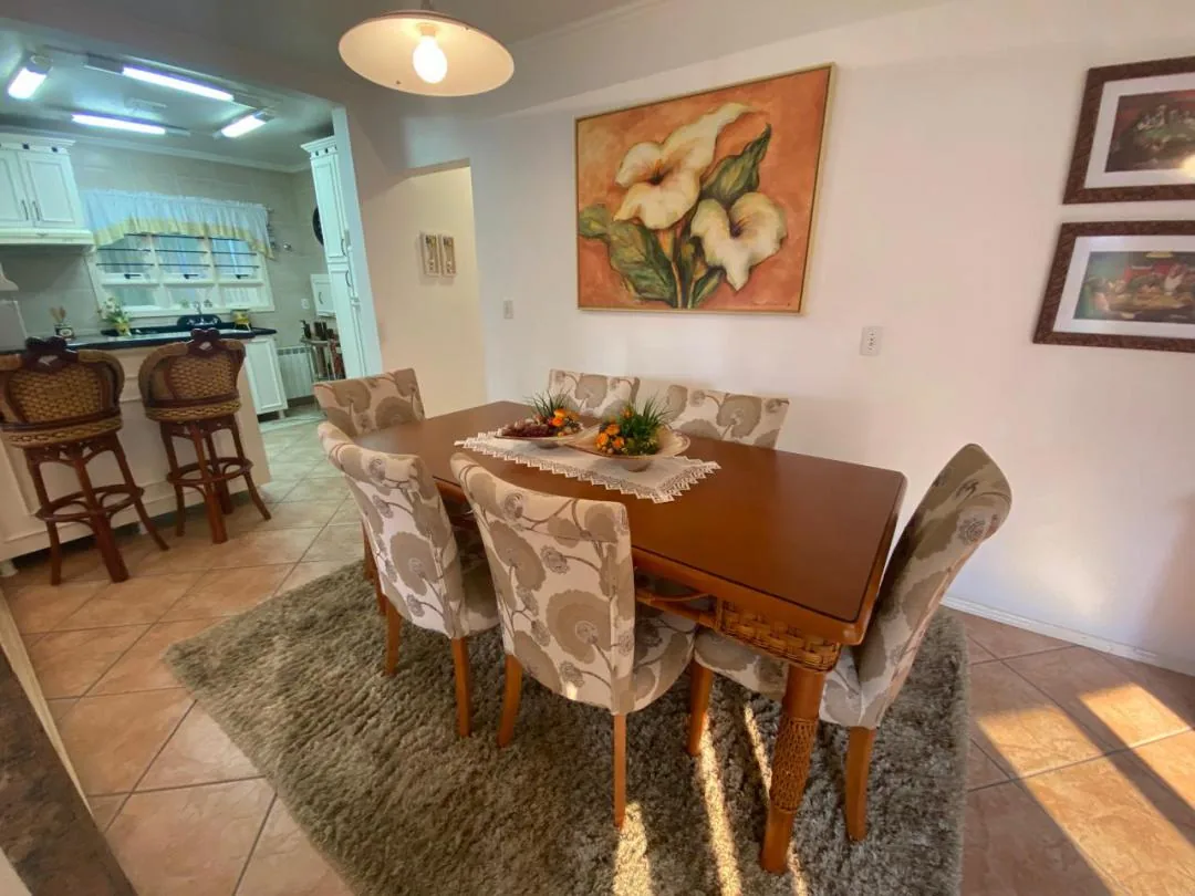 Sala de jantar com mesa de madeira, cadeiras estofadas e balcão com banquetas voltado para a cozinha