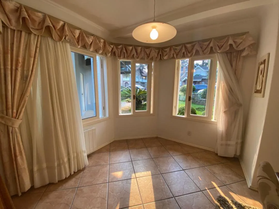 Canto da sala de jantar com três janelas em ângulo, cortinas com bandô e piso cerâmico