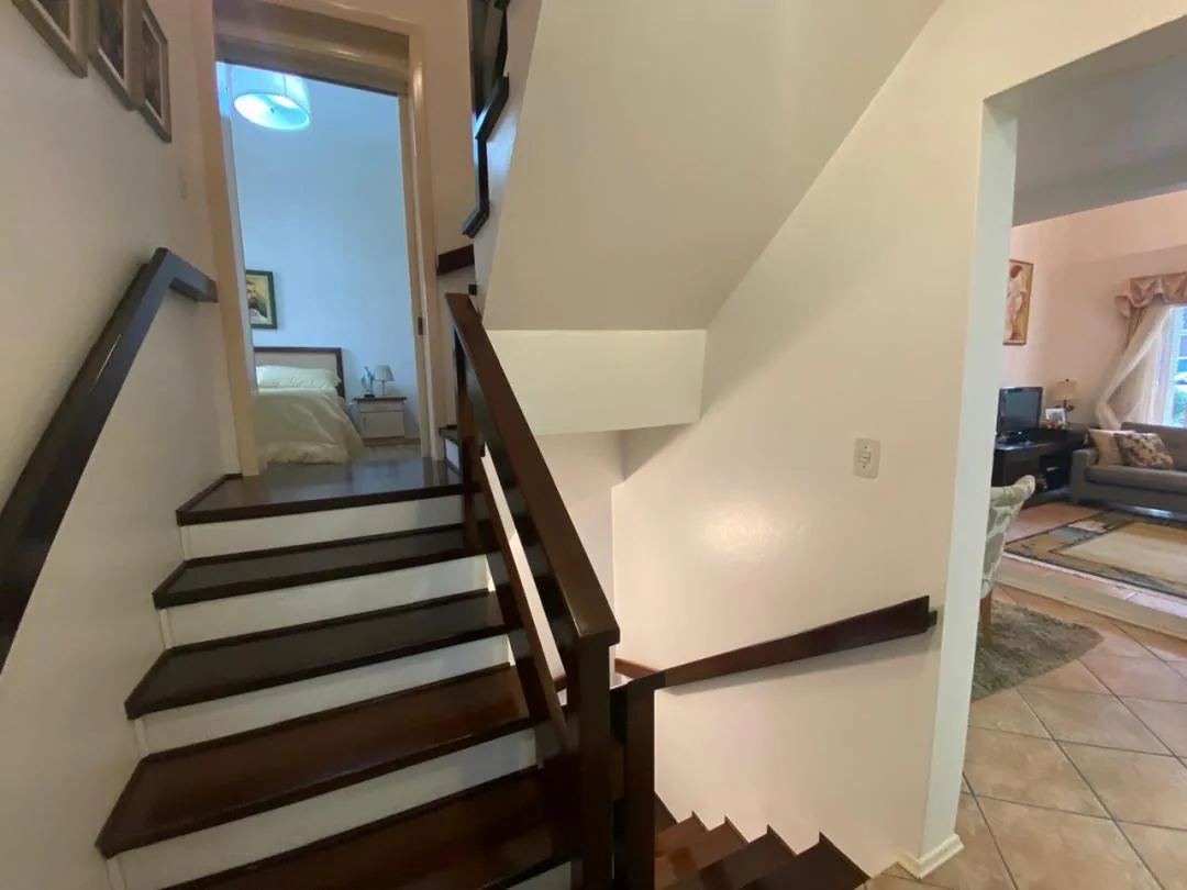 Escada interna com degraus de madeira escura e corrimão, com um quarto ao fundo e a sala embaixo