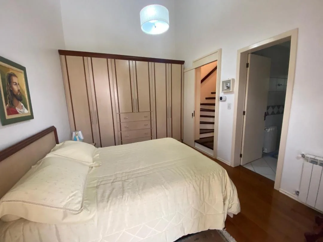 Quarto de casal com roupeiro de madeira, piso de madeira, calefação e porta para o banheiro