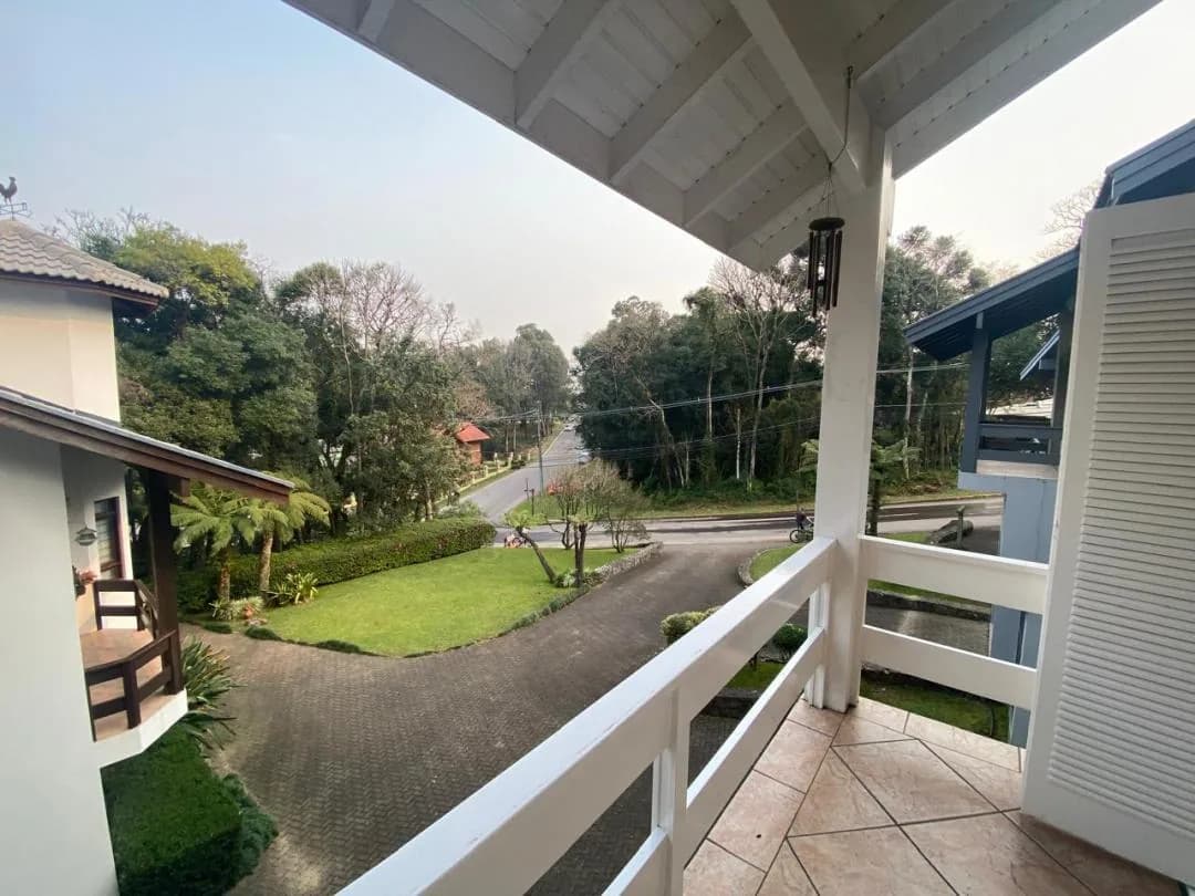 Sacada com guarda-corpo branco e vista para o gramado, a rua e a mata ao redor