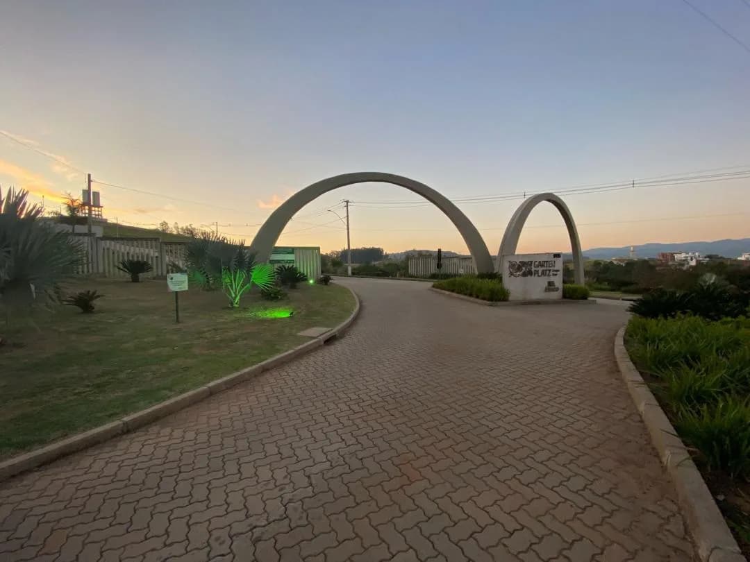 Portal de entrada do loteamento com dois arcos de concreto, monumento com o nome Garten Platz e rua de paver ao entardecer