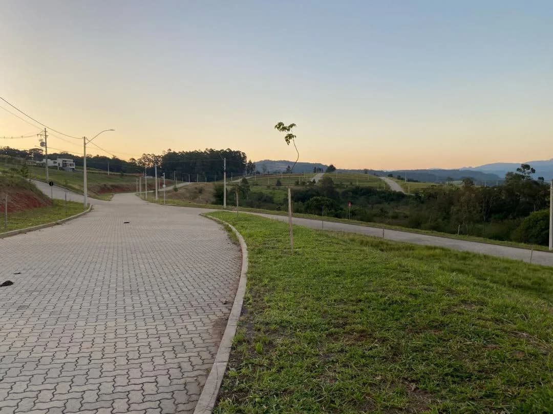 Rua de paver em curva entre gramados, com postes de luz e morros ao fundo