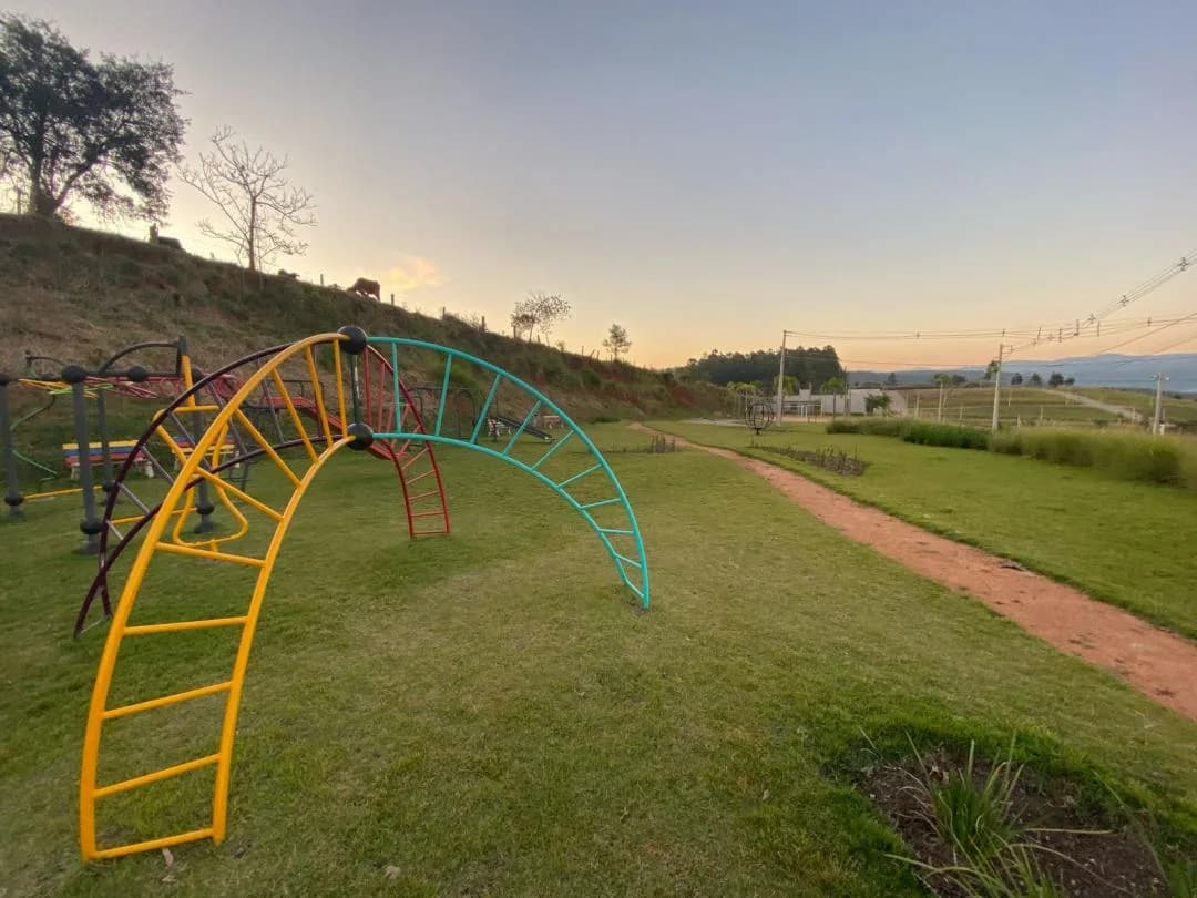 Brinquedos de escalada em arco, amarelo, verde e vermelho, no gramado ao lado de uma trilha de terra