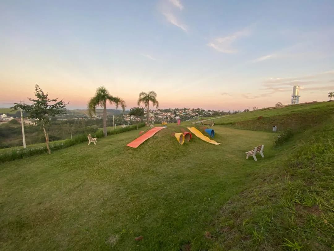 Área gramada com rampas e túneis coloridos, bancos de madeira e vista para a cidade ao entardecer