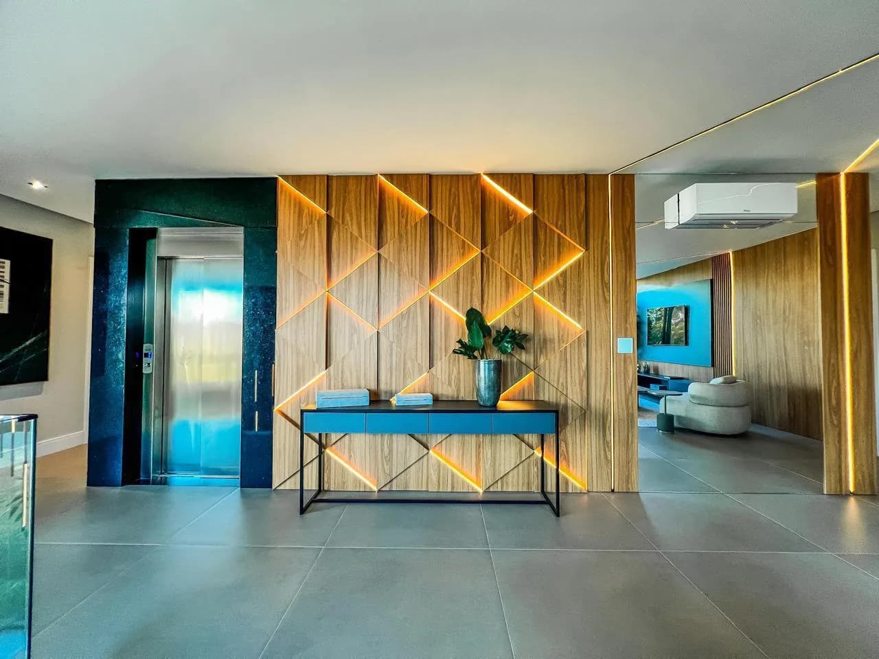 Hall com porta do elevador e painel de madeira com frisos iluminados