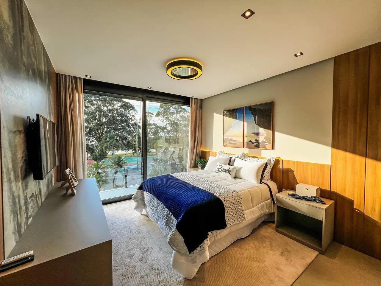 Suíte com cama de casal, cabeceira em painel de madeira e porta de vidro com vista para árvores altas