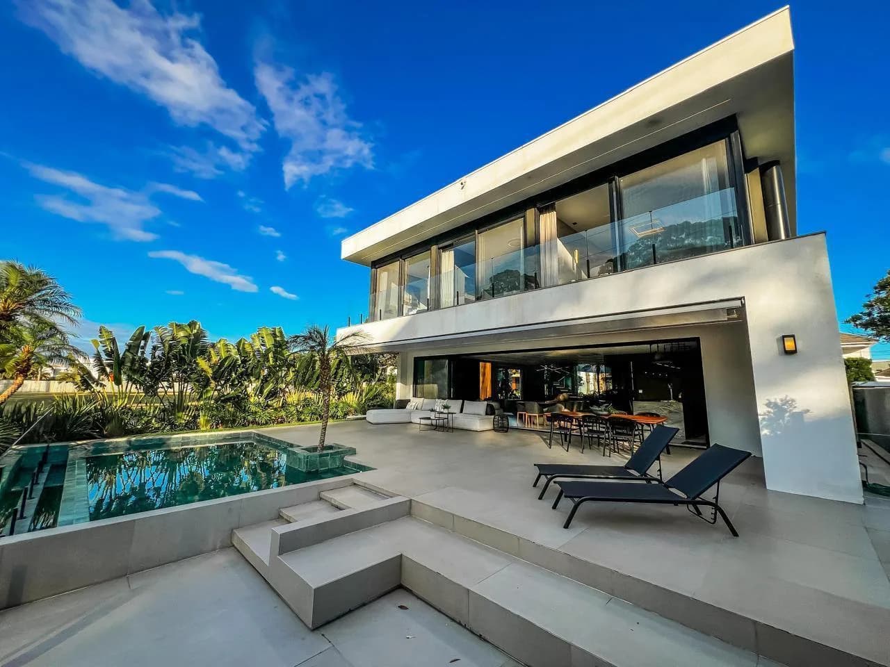 Fundos da casa com terraço, espreguiçadeiras, piscina e varanda aberta para a área gourmet