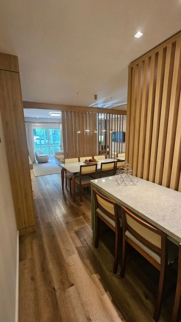 Bancada de pedra com cadeiras junto à mesa de jantar, divisória ripada e a sala com janela ao fundo
