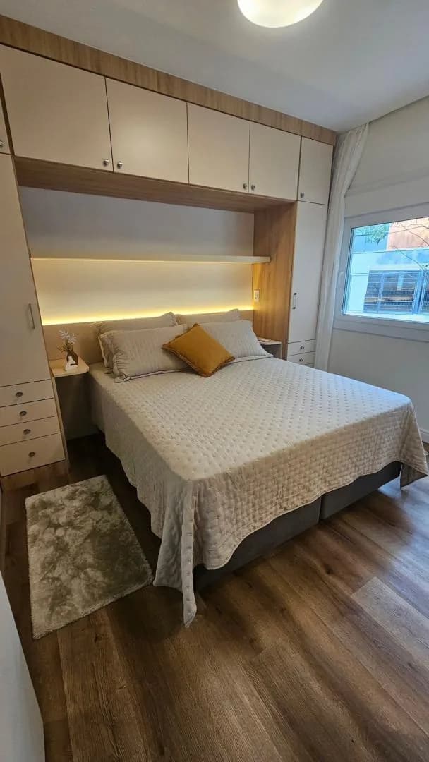 Suíte com cama de casal, cabeceira com luz embutida, armários aéreos brancos e tapete felpudo
