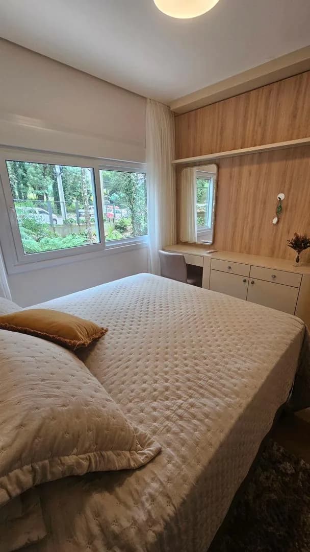 Quarto com cama de casal, escrivaninha com espelho, painel de madeira e janela para o verde