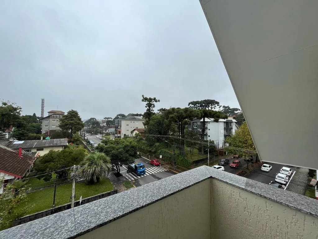 Vista da sacada para a rua arborizada, com araucárias e prédios vizinhos