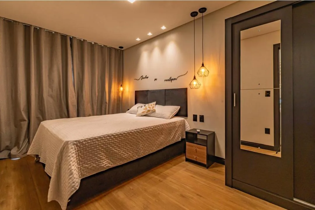 Quarto com cortinas fechadas, cama de casal e guarda-roupa escuro com porta espelhada