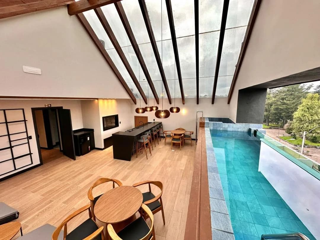 Terraço do prédio com piscina de borda de vidro, mesas de madeira e cobertura de vidro com vigas de madeira