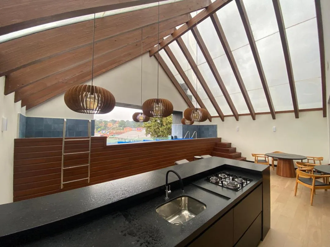 Espaço gourmet no terraço com bancada de granito preto, cooktop e mesas redondas, com a piscina ao fundo