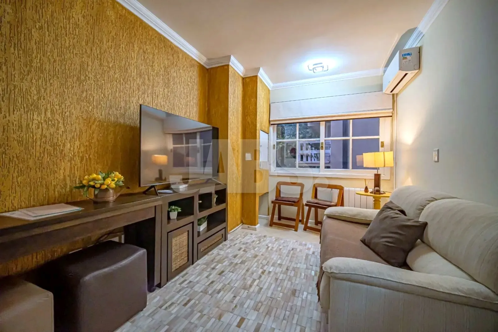 Sala com sofá bege, TV sobre a estante de madeira e parede texturizada dourada