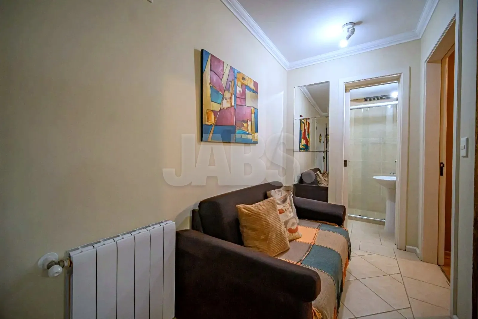 Canto da sala com poltrona, quadro colorido e porta para o banheiro