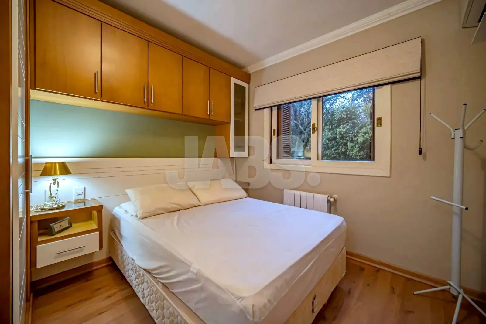 Dormitório com cama de casal, armários aéreos e janela para o verde