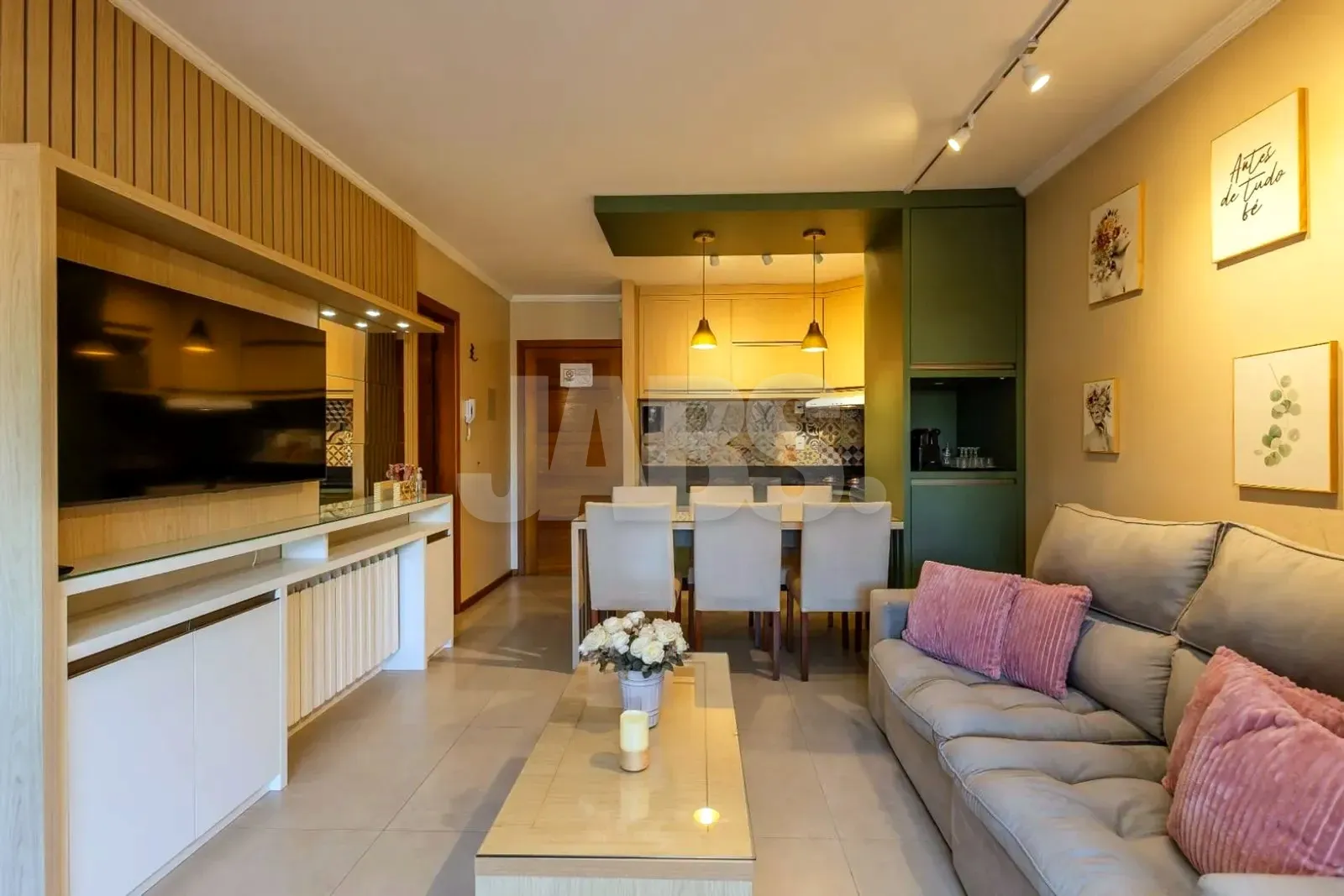 Sala de estar mobiliada com sofá cinza, almofadas rosadas e mesa de jantar junto à cozinha planejada