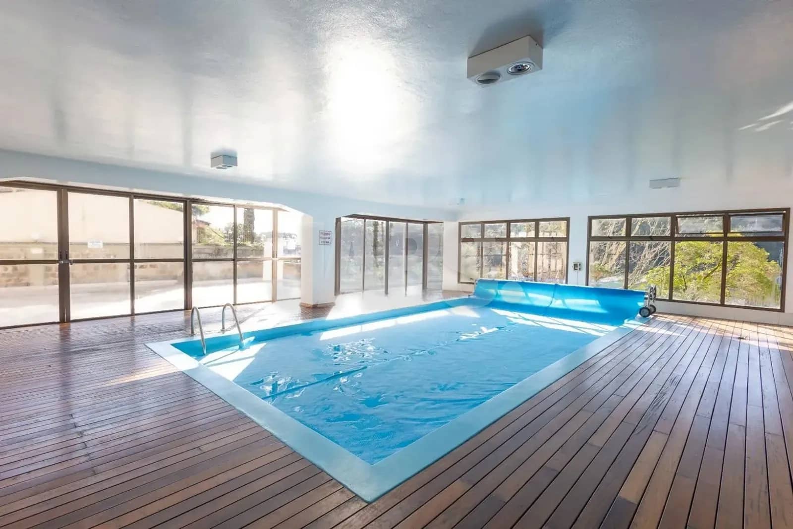 Piscina aquecida coberta com deck de madeira e janelas amplas