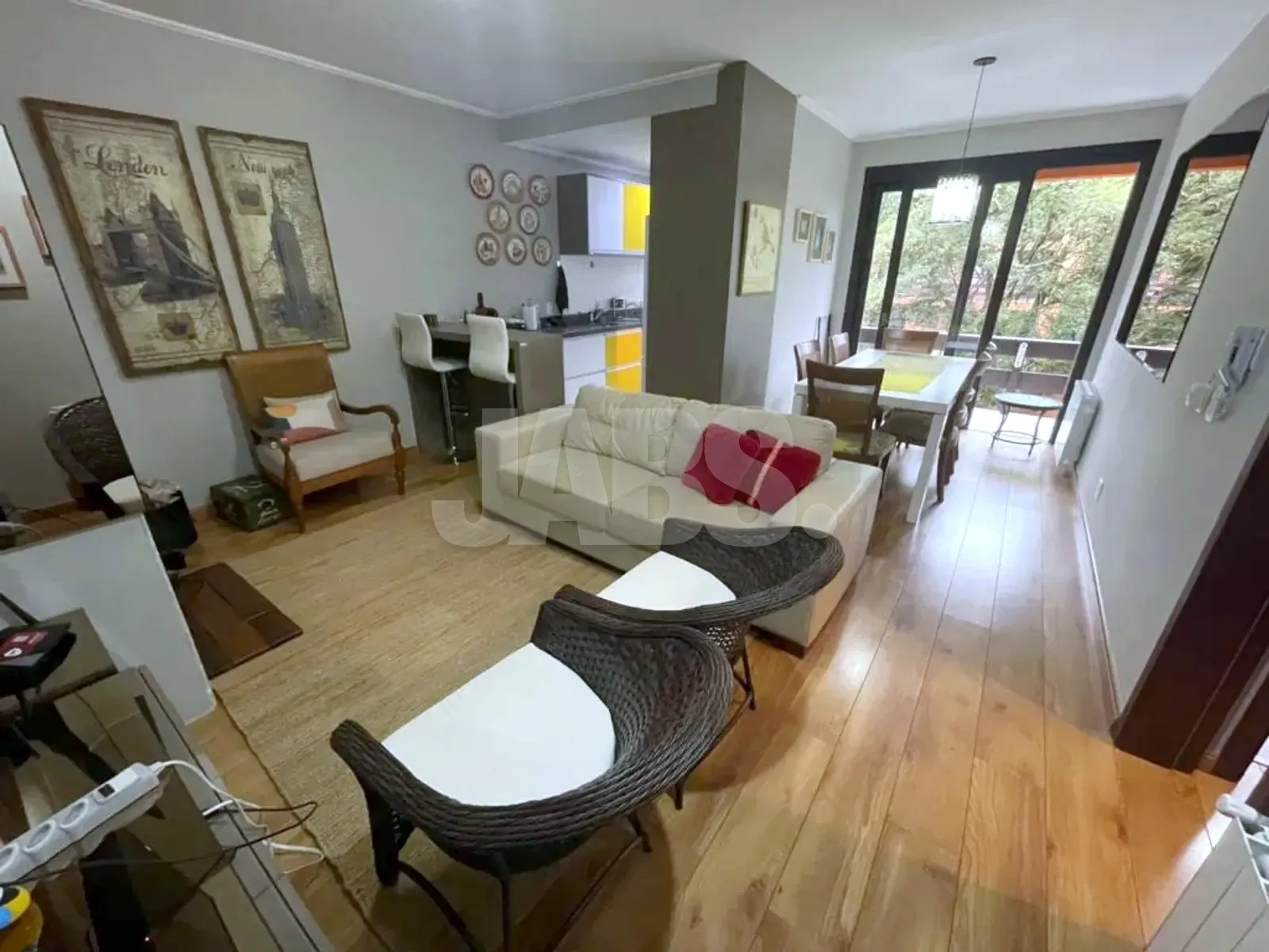 Sala de estar mobiliada com sofá claro, poltronas e mesa de jantar ao fundo junto às janelas para a mata