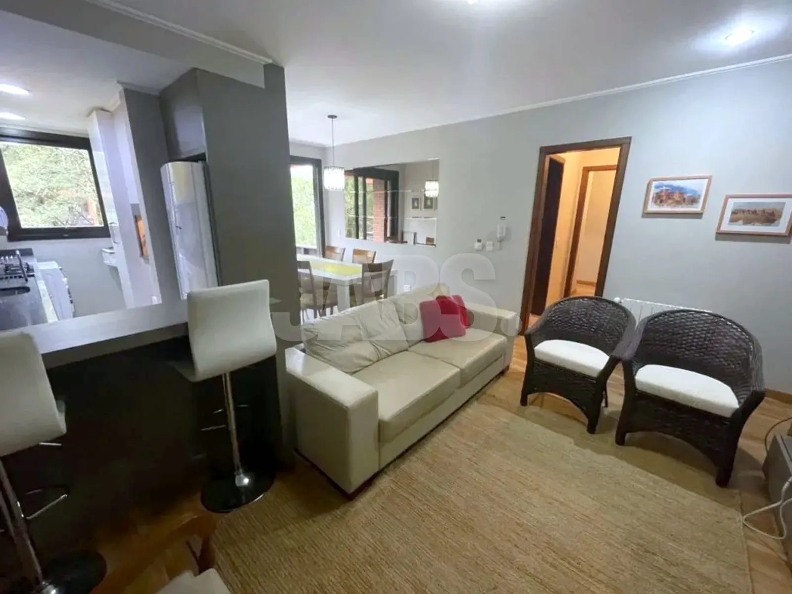 Sala com sofá de três lugares, poltronas de vime e janelas para o verde