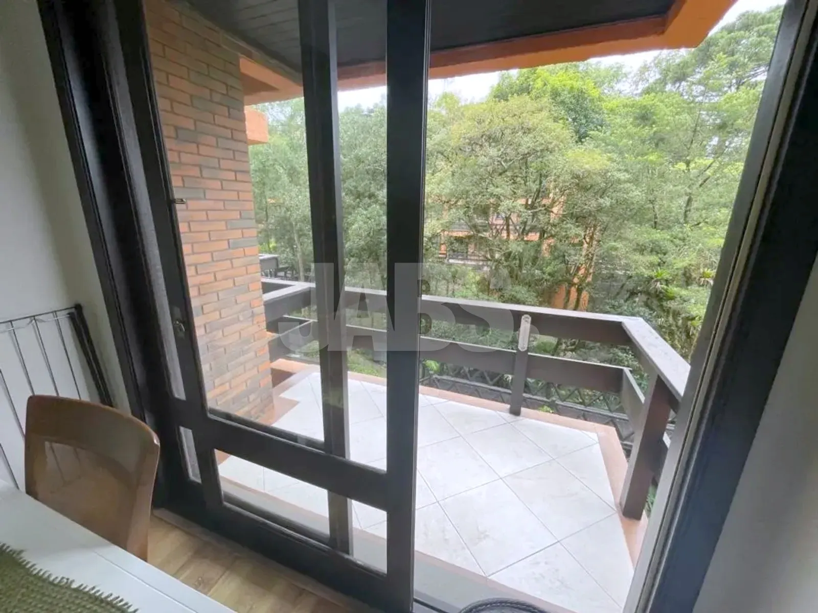 Sacada com guarda-corpo de madeira, piso claro e mata em volta