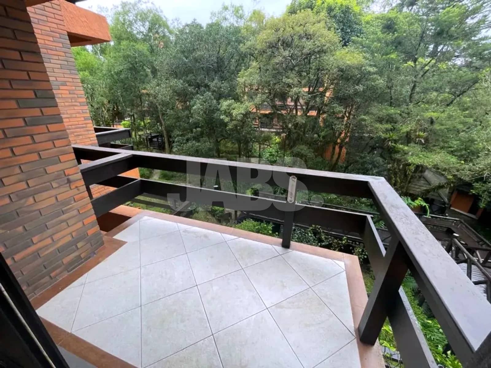 Sacada com parede de tijolos à vista e vista para as árvores do condomínio