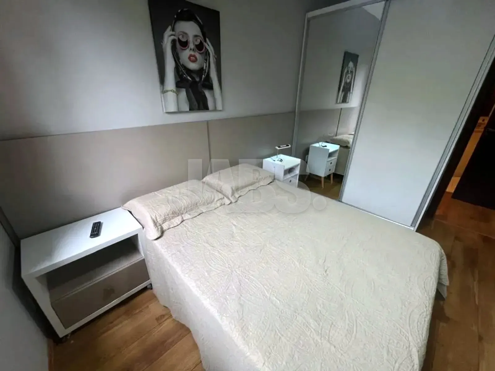 Suíte com cama de casal, quadro na parede e guarda-roupa espelhado