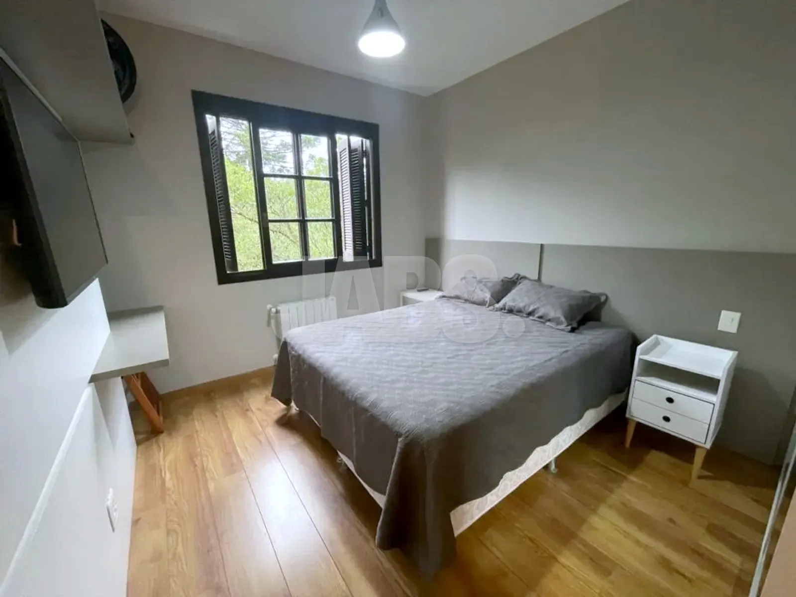 Segundo dormitório com cama de casal, criado-mudo branco e janela de madeira