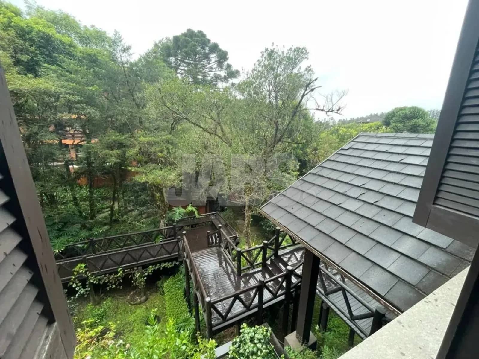 Vista do alto para o jardim do condomínio e a passarela de madeira entre as árvores