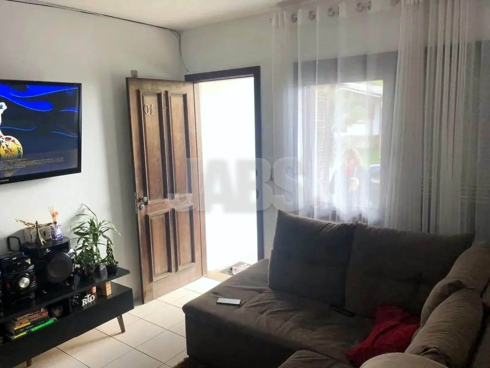 Sala de estar com sofá, porta de madeira maciça e janela com cortina