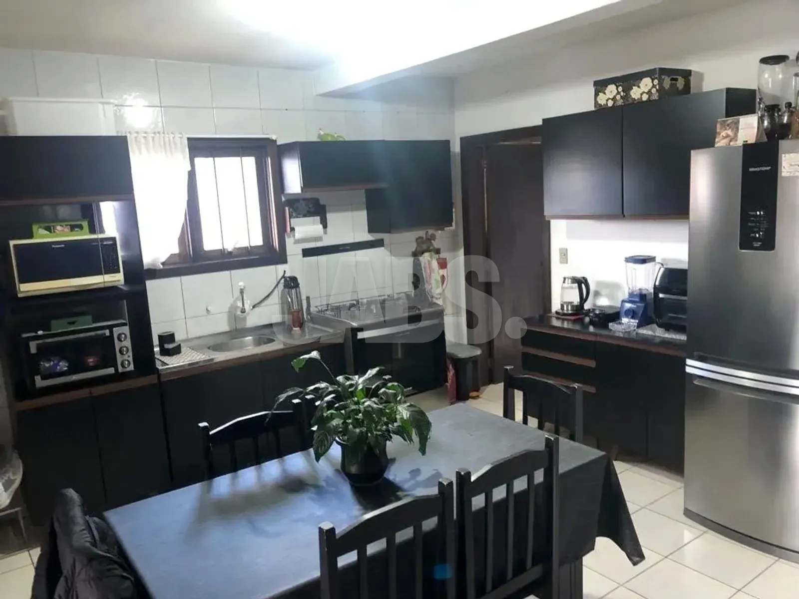 Cozinha com armários planejados escuros, geladeira inox e mesa de jantar