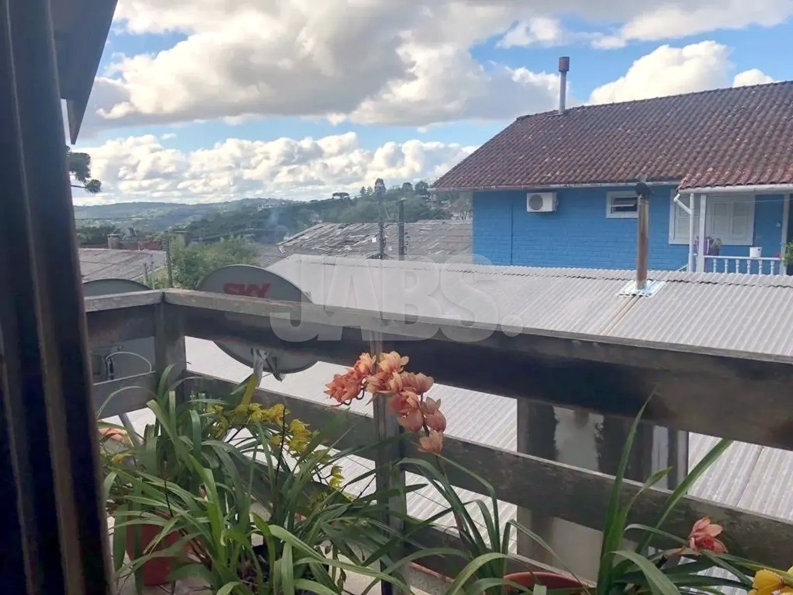 Vista da sacada para o bairro e os morros, com flores na varanda