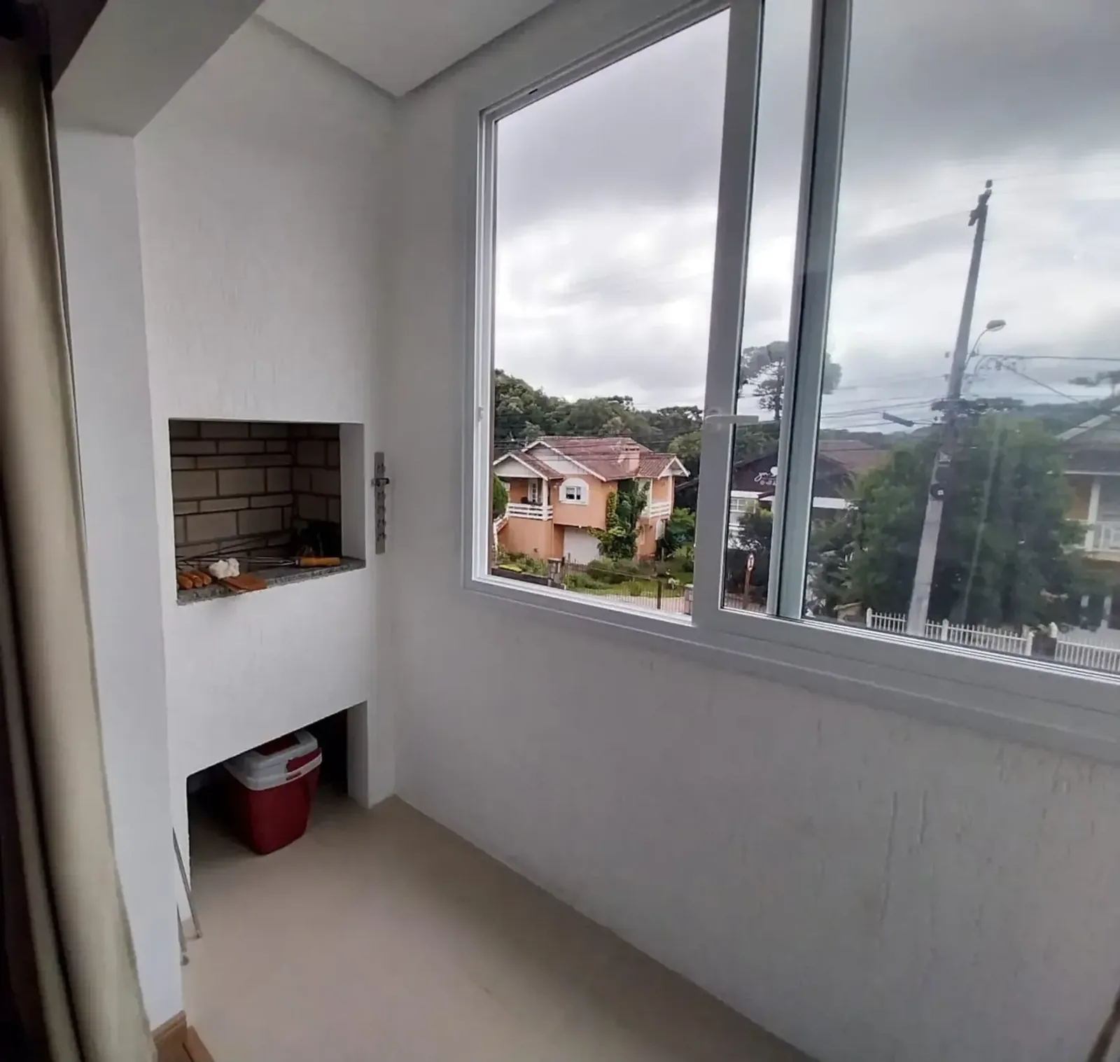 Sacada envidraçada com churrasqueira de tijolos e vista para as casas do bairro