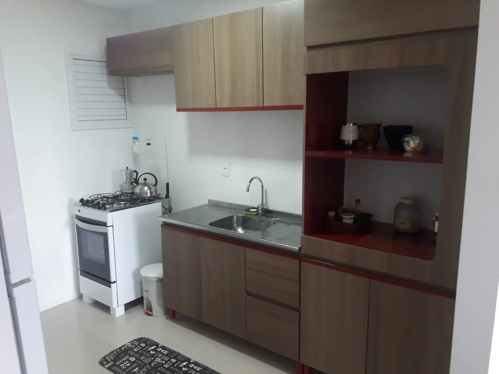 Cozinha com armários amadeirados, fogão branco, pia de inox e nichos com louças
