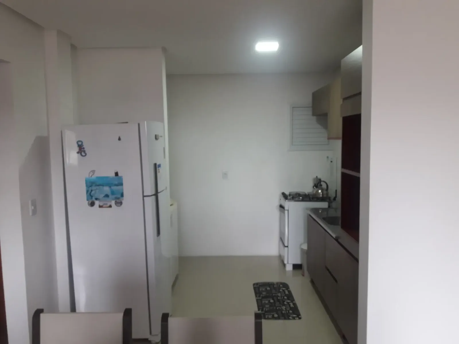 Cozinha americana com geladeira branca e armários amadeirados vista da sala