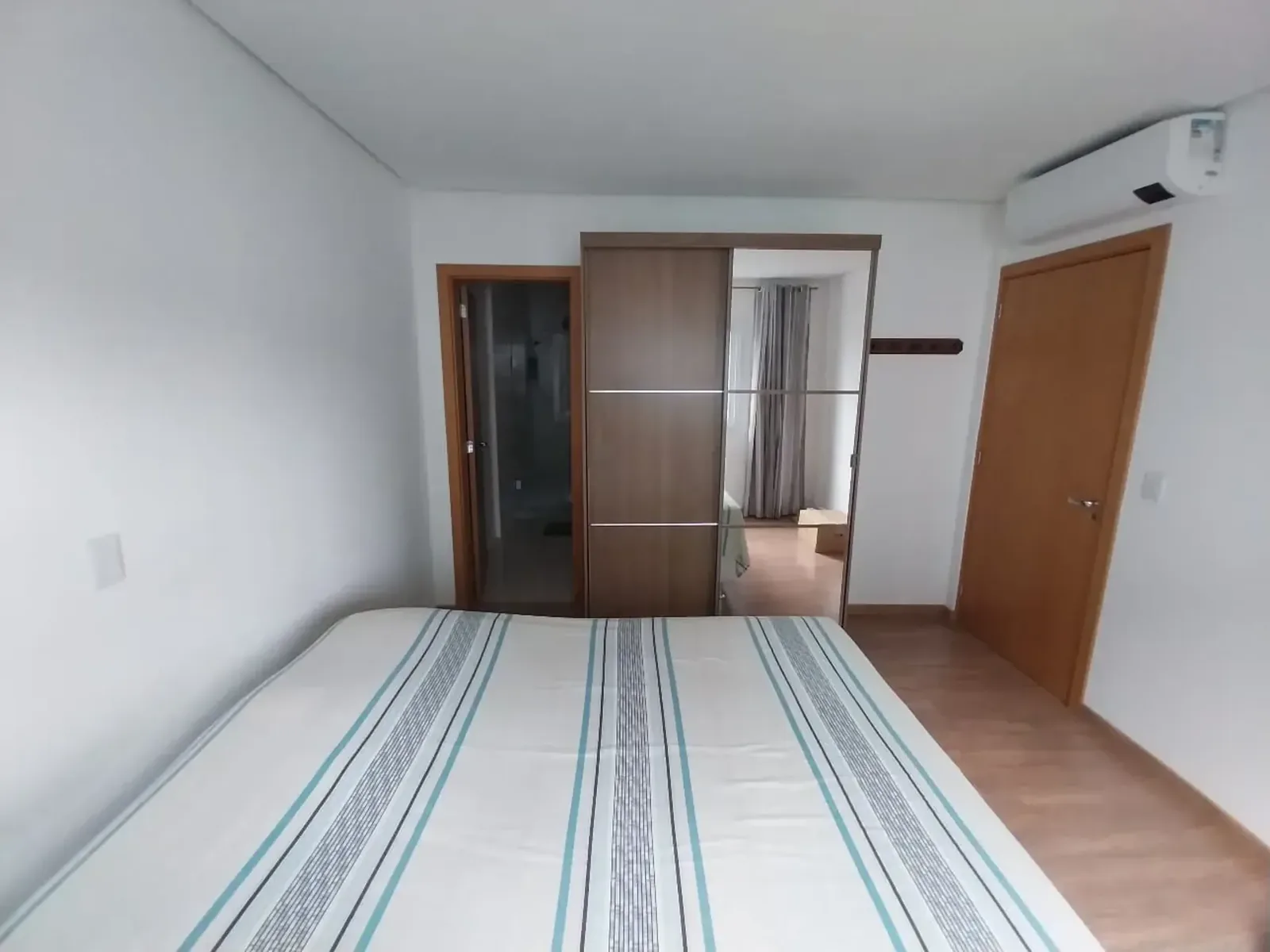 Dormitório com cama de casal, guarda-roupa de portas de correr, ar-condicionado split e portas de madeira