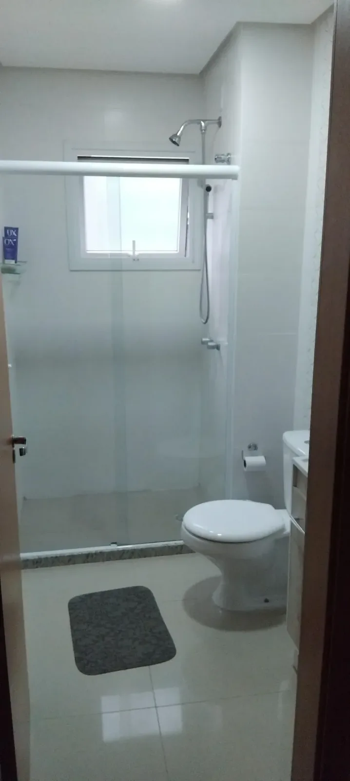Banheiro com box de vidro, vaso sanitário e tapete