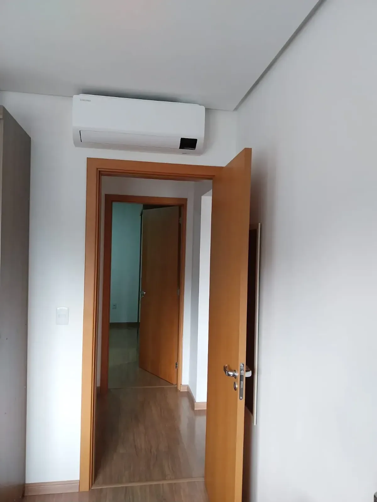 Corredor com ar-condicionado split e portas de madeira para os dormitórios