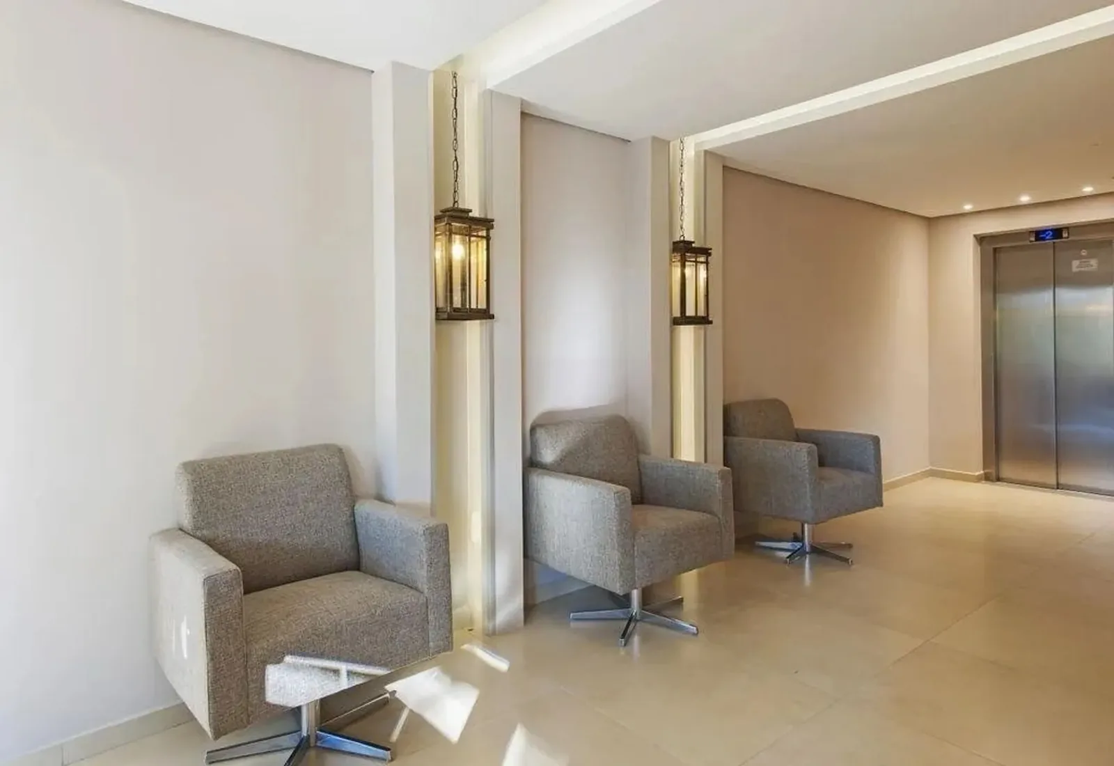 Hall de entrada com poltronas, arandelas e porta do elevador