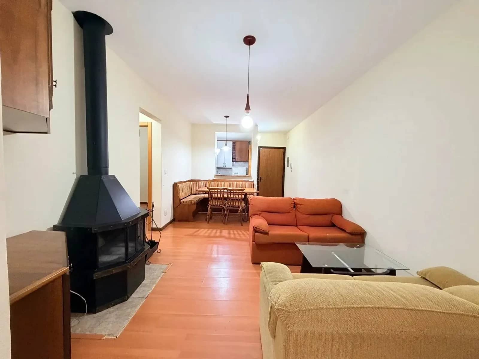 Sala com lareira preta, sofás laranja e bege e mesa de jantar com banco de canto ao fundo