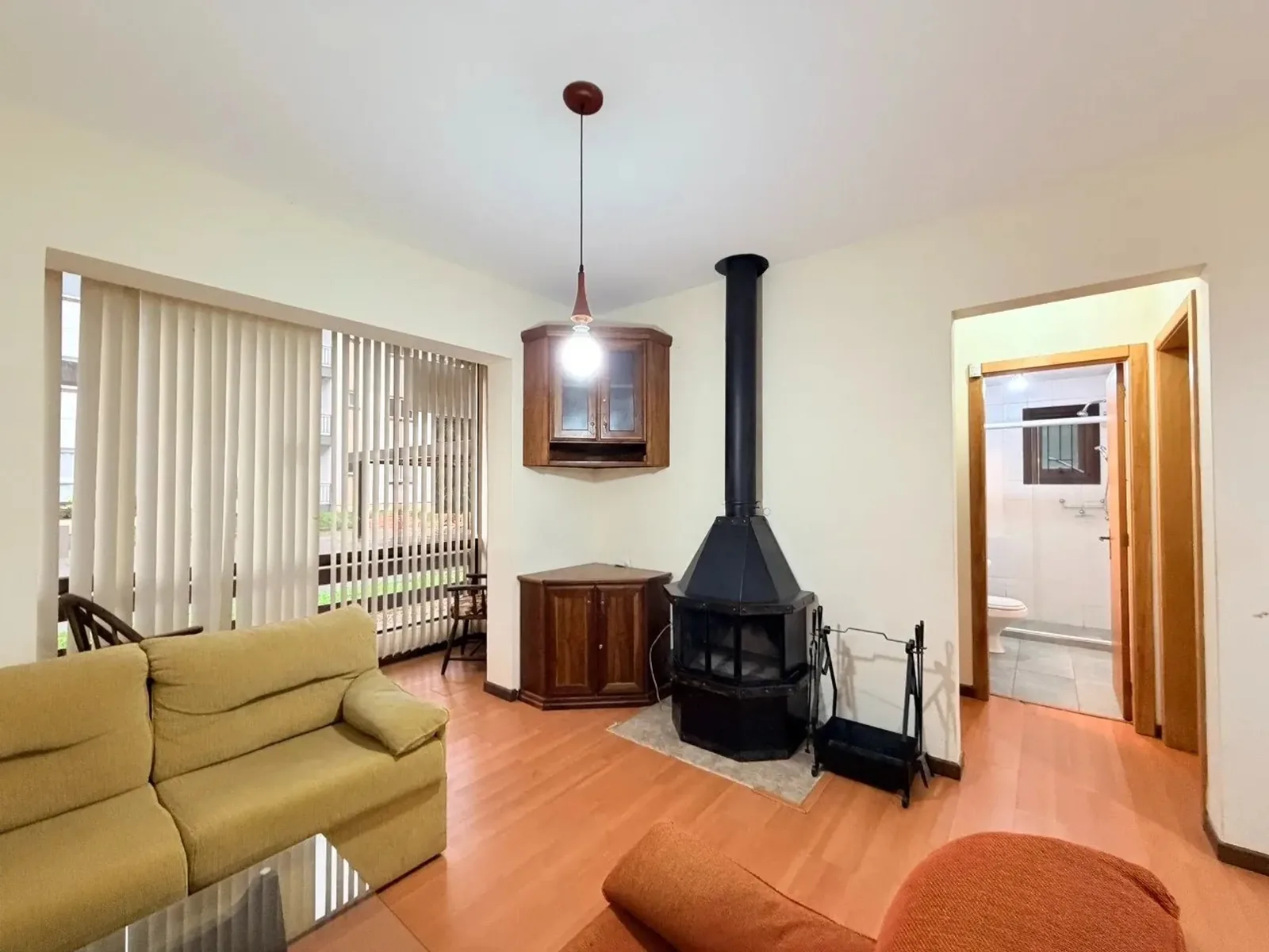 Canto da sala com lareira de ferro, cristaleira de madeira e porta da sacada com persianas