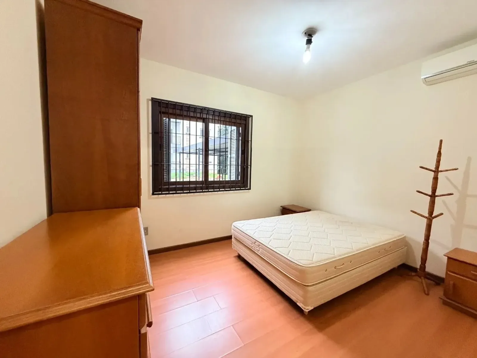 Dormitório com cama de casal, janela gradeada e guarda-roupa de madeira