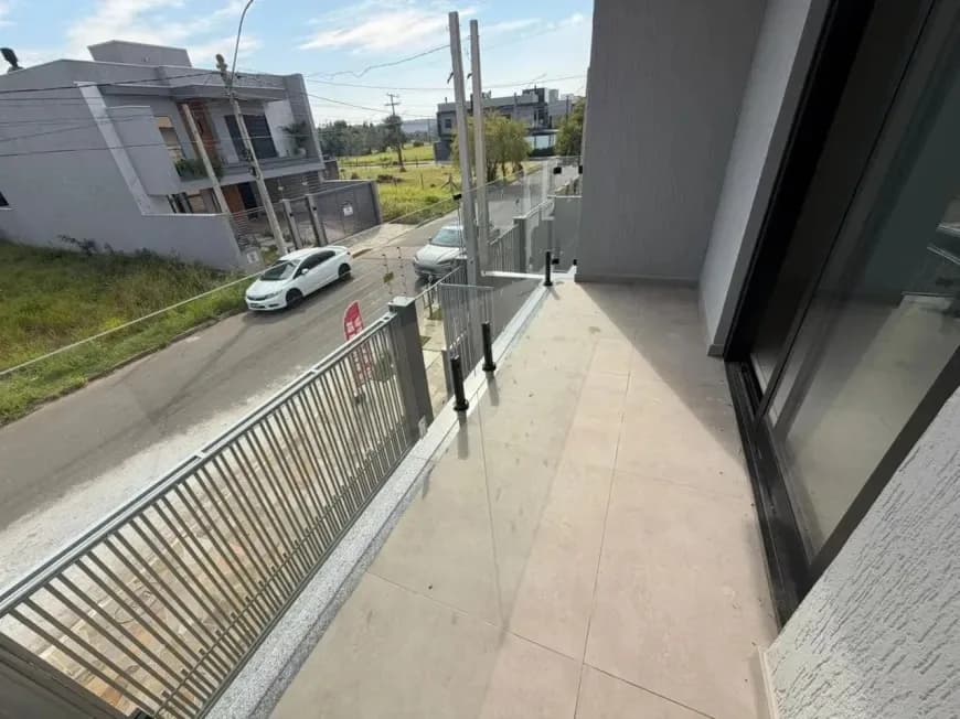 Varanda do andar superior com guarda-corpo de vidro, vista da rua e carros estacionados