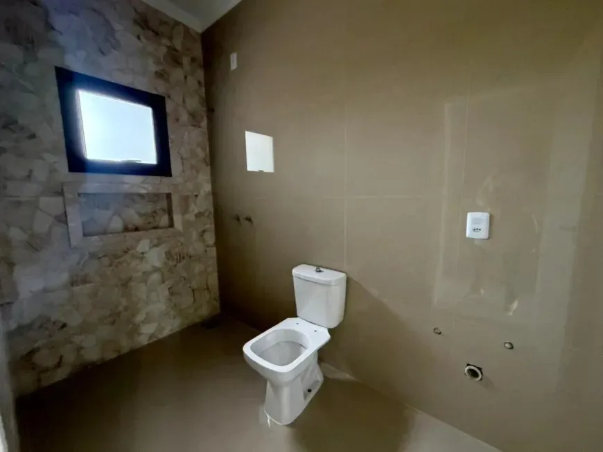 Lavabo com vaso sanitário e revestimento em pedra, com janela pequena