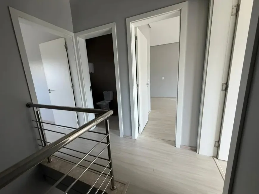 Corredor do andar superior com portas abertas para o banheiro e um dos dormitórios, corrimão de inox